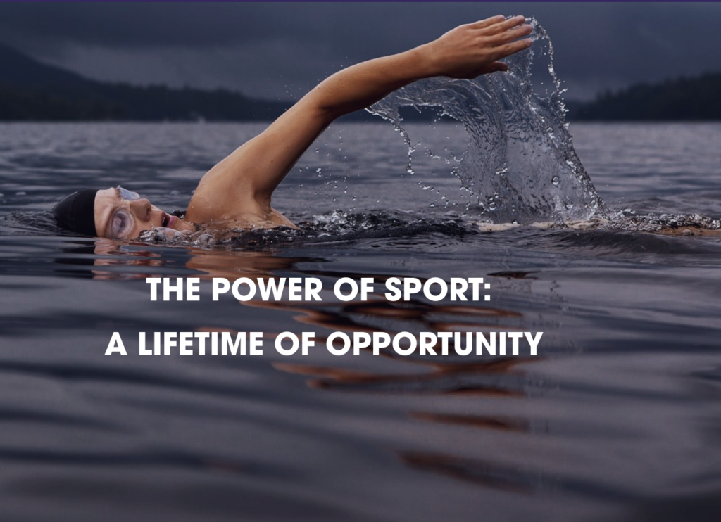 A swimmer with a swim cap and goggles is doing front crawl in a calm lake, surrounded by forested hills. Water splashes as the swimmer's arm cuts through it. The text in the center reads, "THE POWER OF SPORT: A LIFETIME OF OPPORTUNITY.